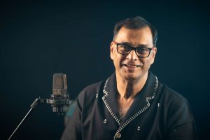 Chancellor Phalguni Mookhopadhayay singing Bangla Gaan with a studio microphone.